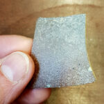 Auf diesem Bild sieht man eine Keramikscherbe mit einem braunen, leicht glänzendem Überzug.